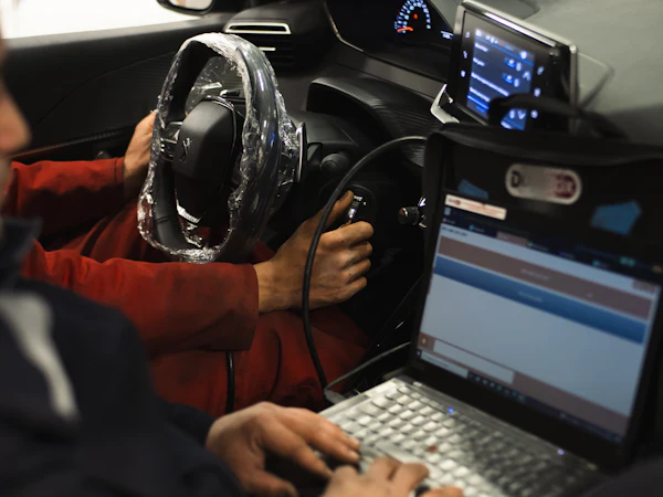 Mekaniker sidder i bilen og læser fejlkoder på en bærbar computer